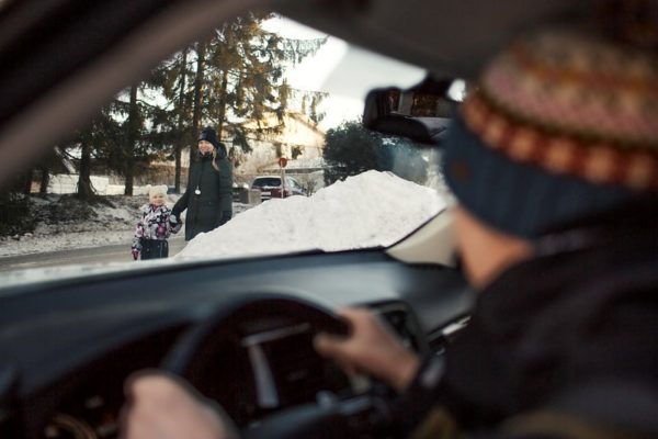 Autoilija katsoo lumivallin takana olevaa lasta ja aikuista